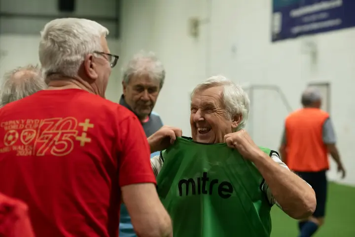 Ältere Herren beim Hallenfußball, einer zieht lachend ein grünes Leibchen über