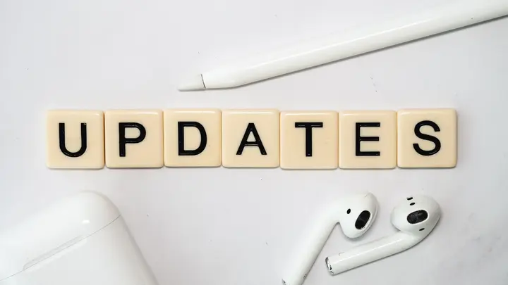 Buchstabensteine bilden das Wort „UPDATES“, daneben ein Stift und kabellose Kopfhörer